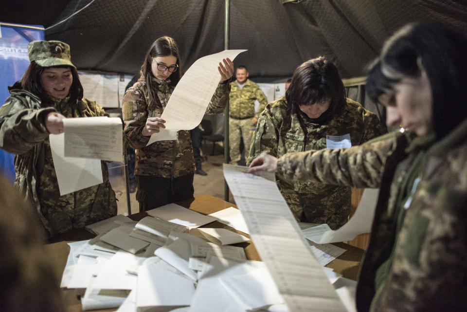 Ukrainian government soldiers, members of the local election commission count ballots in a tent used as a polling station during the presidential elections in Mariinka, near a contact line not far from Donetsk, eastern Ukraine, Sunday, March 31, 2019. Volodymyr Zelenskiy, the comedian and actor whom exit polls show leading Ukraine's presidential election, said Sunday he has made a major step toward victory. (AP Photo/Evgeniy Maloletka)