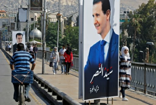 People walk near a portrait of Syrian President Bashar al-Assad hanging in a street in the Syrian capital Damascus on May 31, 2018