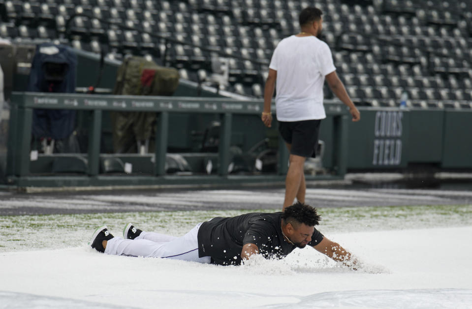 Colorado Rockies catcher Elias Diaz, front, dives onto a hail-covered tarpaulin after a summer storm packing heavy rain, high winds and large hail swept over Coors Field, Thursday, June 29, 2023, in Denver. Injured Rockies pitcher German Marquez, back, walks away. The Rockies were set to host the Los Angeles Dodgers, Thursday. (AP Photo/David Zalubowski)