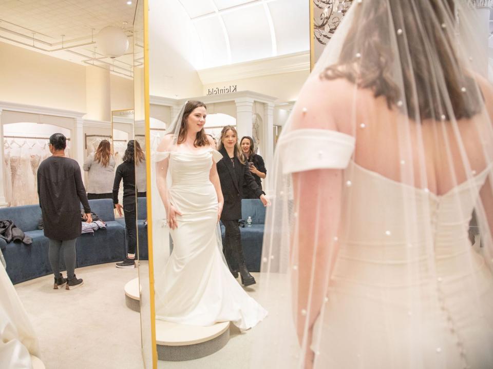 A woman in a wedding dress looks at herself in a mirror.