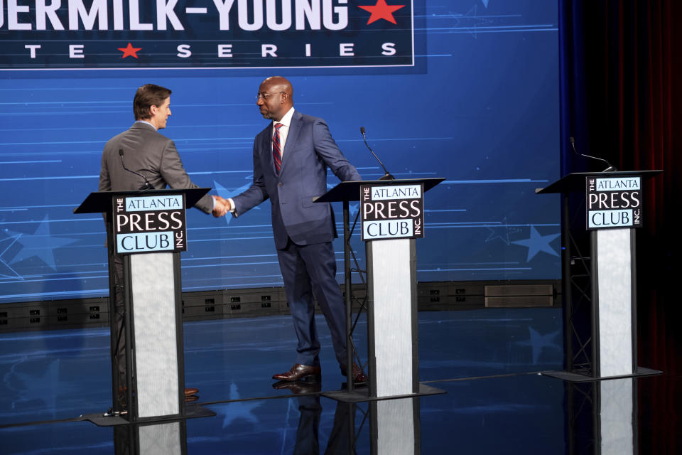 Libertarian challenger Chase Oliver, left, and U.S. Sen. Raphael Warnock, D-Ga., shake hands following the Atlanta Press Club Loudermilk-Young Debate Series in Atlanta, for the U.S. Senate race, Sunday, Oct. 16, 2022. The empty podium at right was for Republican challenger Herschel Walker, who was invited but did not attend. (AP Photo/Ben Gray)