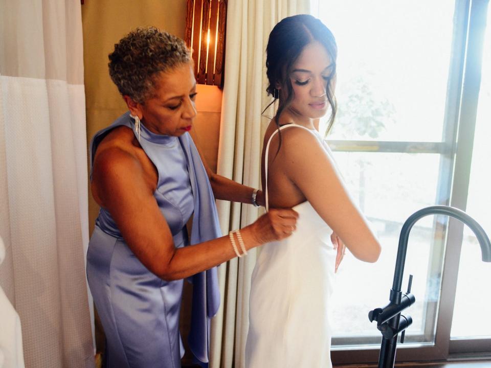 A woman adjusts another woman's wedding dress.