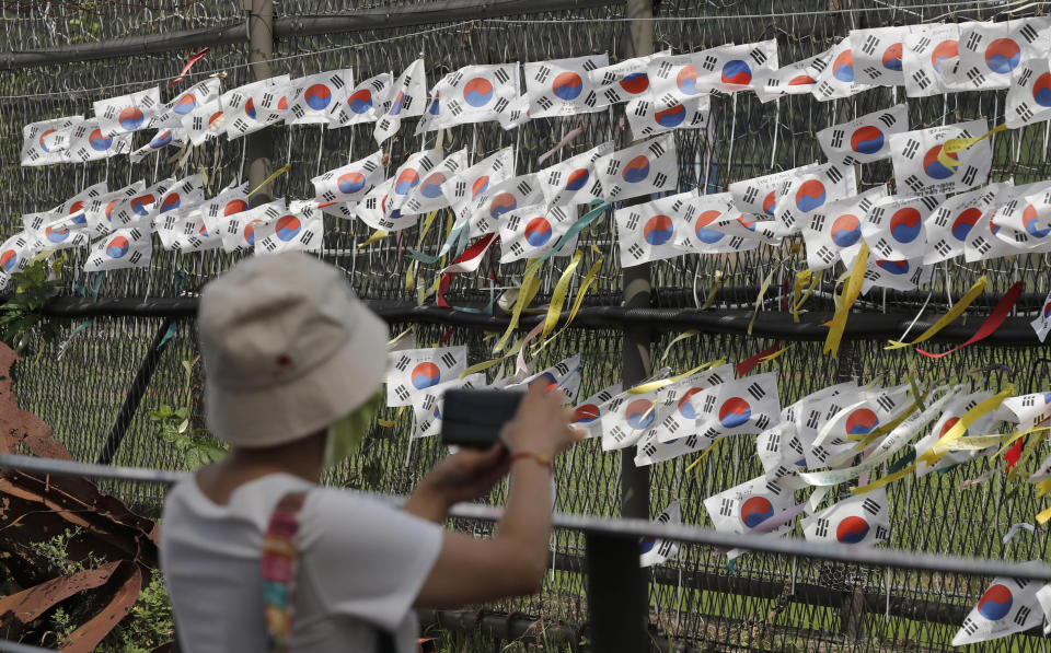 A visitor takes photos near the wire fence decorated with South Korean national flags and ribbons written with messages wishing for the reunification of the two Koreas at the Imjingak Pavilion in Paju, South Korea, Sunday, Aug. 11, 2019. North Korea said Sunday leader Kim Jong Un supervised test-firings of an unspecified new weapons system, which extended a streak of launches that are seen as an attempt to build leverage ahead of negotiations with the United States while driving a wedge between Washington and Seoul. (AP Photo/Lee Jin-man)