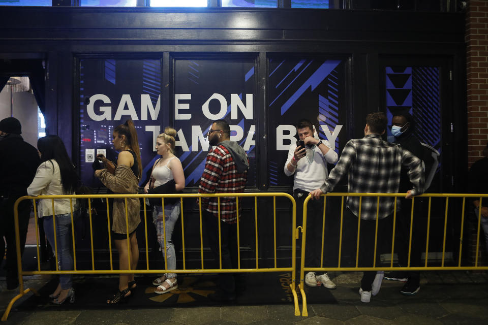 People stand close to one another in line along yellow fencing outside a venue, most without face masks