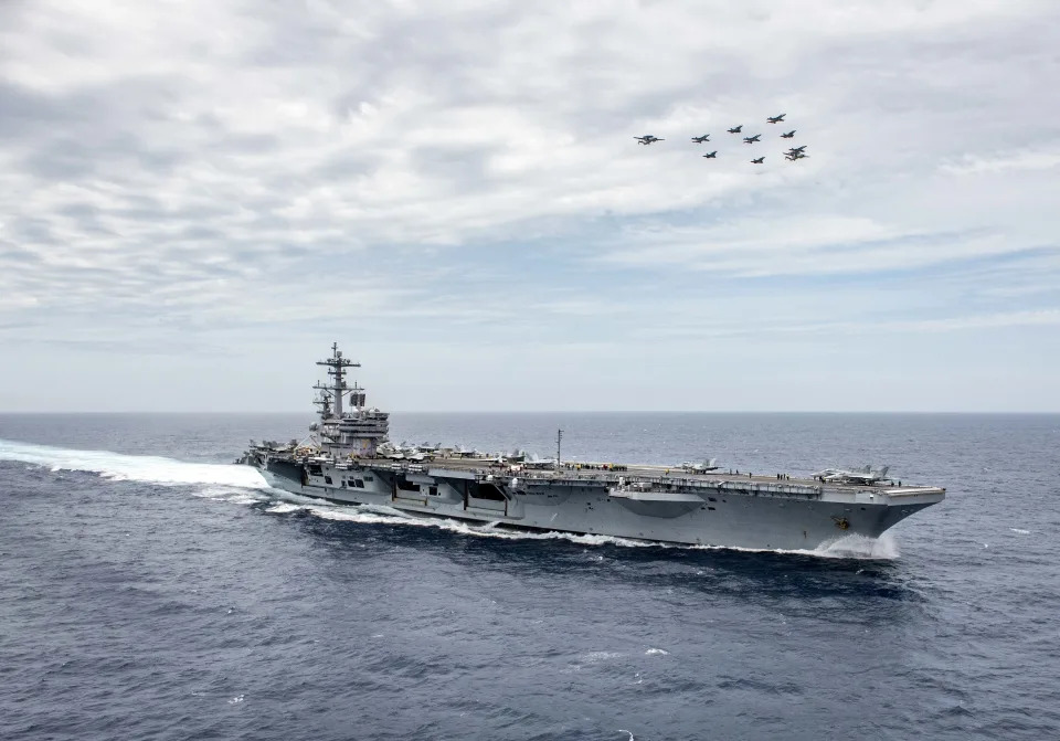 Aircraft are seen flying in formation over the aircraft carrier USS George HW Bush