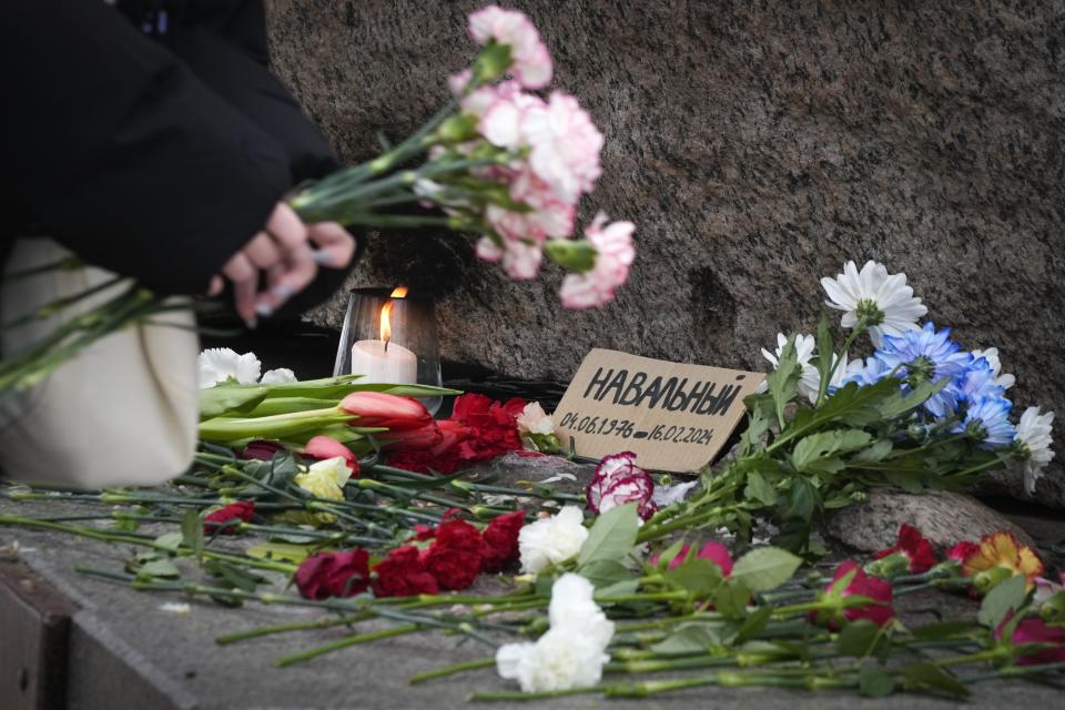 A woman pays tribute to Alexei Navalny at the monument, a large boulder from the Solovetsky islands, where the first camp of the Gulag political prison system was established in St. Petersburg, Russia, on Wednesday, Feb. 21, 2024. Russians across the vast country streamed to ad-hoc memorials with flowers and candles to pay tribute to Alexei Navalny, the most famous Russian opposition leader and the Kremlin's fiercest critic. Russian officials reported that Navalny, 47, died in prison on Friday, Feb. 16, 2024. (AP Photo/Dmitri Lovetsky)