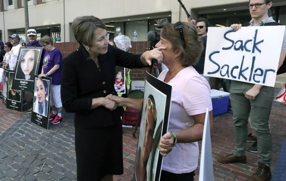 FILE - In this Aug. 2, 2019, file photo, Massachusetts Attorney General Maura Healey, left, wipes a tear from the face of Wendy Werbiskis, of East Hampton, Mass., one of the protesters gathered outside a courthouse in Boston, where a judge was to hear arguments in the state's lawsuit against Purdue Pharma over its role in the national drug epidemic. Reports emerging about a possible financial settlement with Purdue, the company that has come to symbolize the nation's opioid epidemic, suggests the settlement amount won't come anywhere near what the national crisis has cost. (AP Photo/Charles Krupa, File)