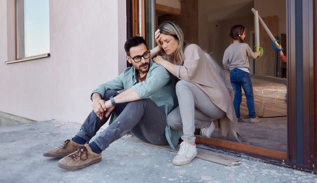 <p>Getty</p> Stock image of tired parents sitting in door while kids play inside house