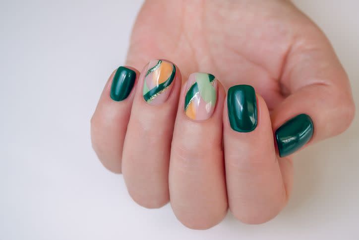 female hands with a manicure with green and orange gel polish with the addition of gold