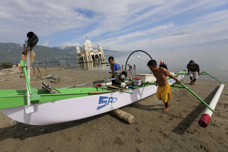 In this April 3, 2019, photo, local fishermen pull a boat to the beach as a mosque heavily damaged by the 2018 earthquake and tsunami is seen in the background in Palu, Central Sulawesi, Indonesia. Indonesia's Islamic Defenders Front is better known for vigilante actions against gays, Christmas decorations and prostitution, but over the past decade and a half it has repurposed its militia into a force that's as adept at searching for victims buried under earthquake rubble and distributing aid as it is at inspiring fear. (AP Photo/Tatan Syuflana)