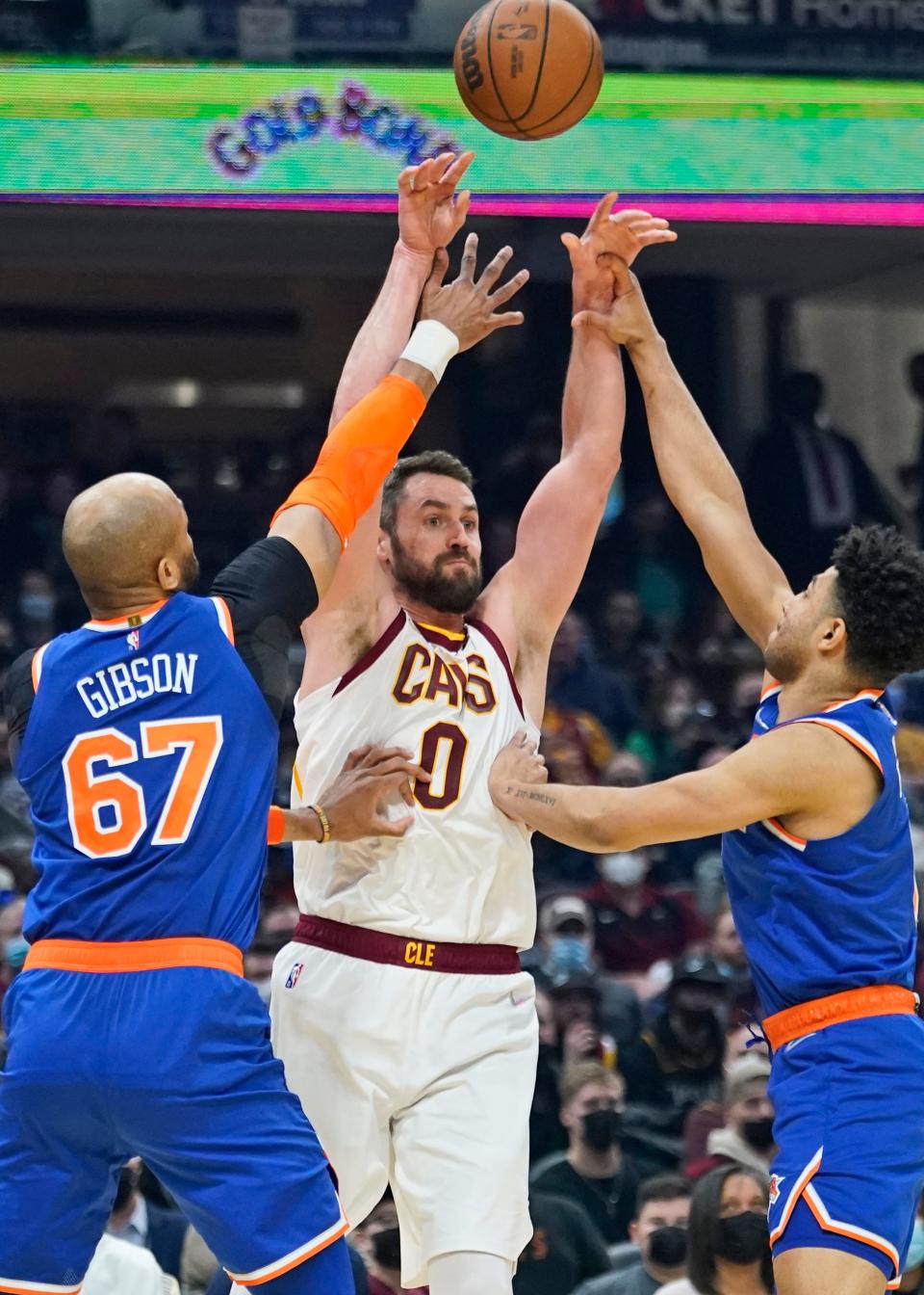 Cleveland Cavaliers' Kevin Love (0) passes over New York Knicks' Taj Gibson (67) and Quentin Grimes (6) in the first half of an NBA basketball game, Monday, Jan. 24, 2022, in Cleveland. (AP Photo/Tony Dejak)