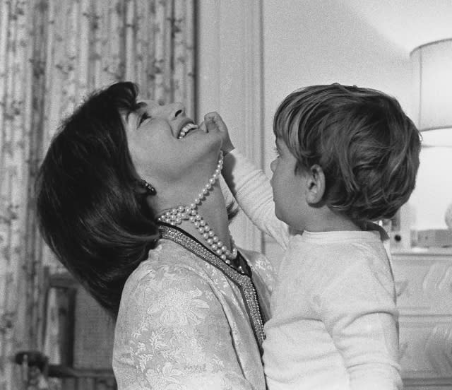 First Lady Jacqueline Kennedy laughs as her son John Kennedy Jr. plays with her simulated-pearl necklace in White House nursery. Nov. 27, 1962