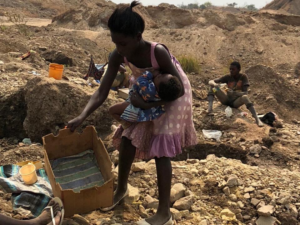 A woman places a baby into a cardboard crib on the ground while she works at a cobalt mine site. Women are paid only a fraction of the paltry sums paid to men for their mining work (Siddharth Kara)