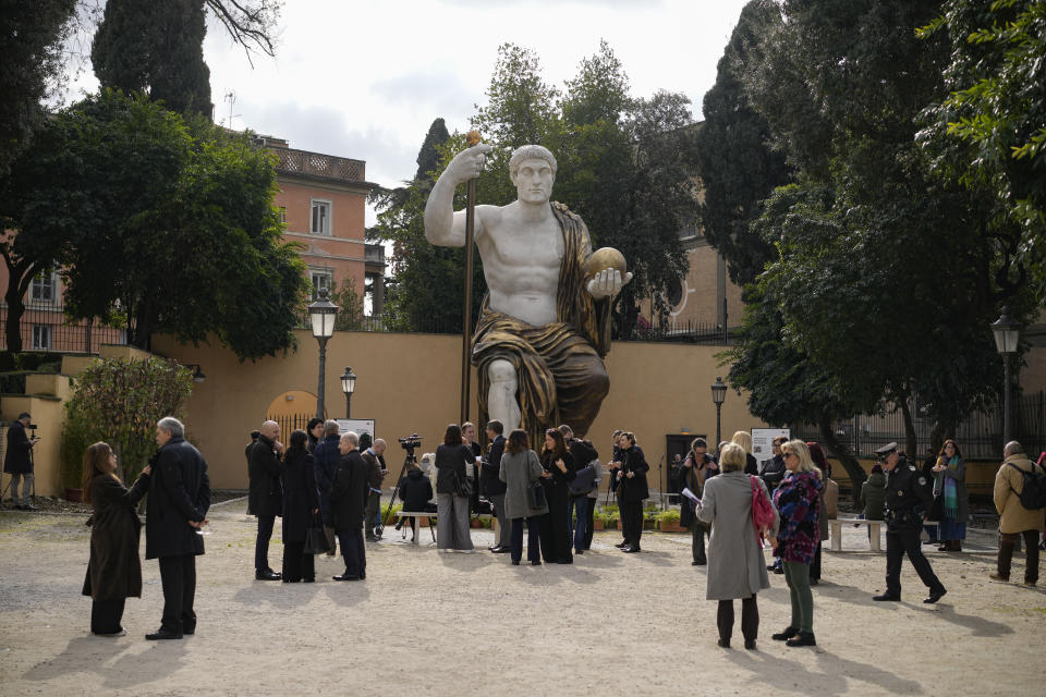 Visitors admire a massive, 13-meter (yard) replica of the statue Roman Emperor Constantine commissioned for himself after 312 AD that was built using 3D technology from scans of the nine giant original marble body parts that remain, as it was unveiled in Rome, Tuesday, Feb. 6, 2024. The imposing figure of a seated emperor, draped in a gilded tunic and holding a scepter and orb, gazing out over his Rome, is located in a side garden of the Capitoline Museums, just around the corner from the courtyard where the original fragments of Constantine's giant feet, hands and head are prime tourist attractions. (AP Photo/Andrew Medichini)