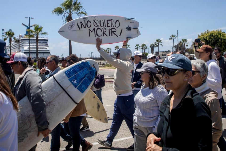 Un manifestante sostiene una tabla de bodyboard con la leyenda “¡No quiero morir!” mientras protesta por los asesinatos de surfistas extranjeros en Ensenada, México (AP)