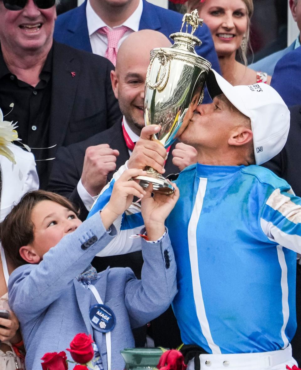 Javier Castellano kisses the Derby trophy as son Brady helps hold after the jockey and Mage won the 149th Kentucky Derby Saturday at Churchill Downs in Louisville, Ky. Behind them is Mage owner Ramiro Restrepo.  May, 6, 2023.