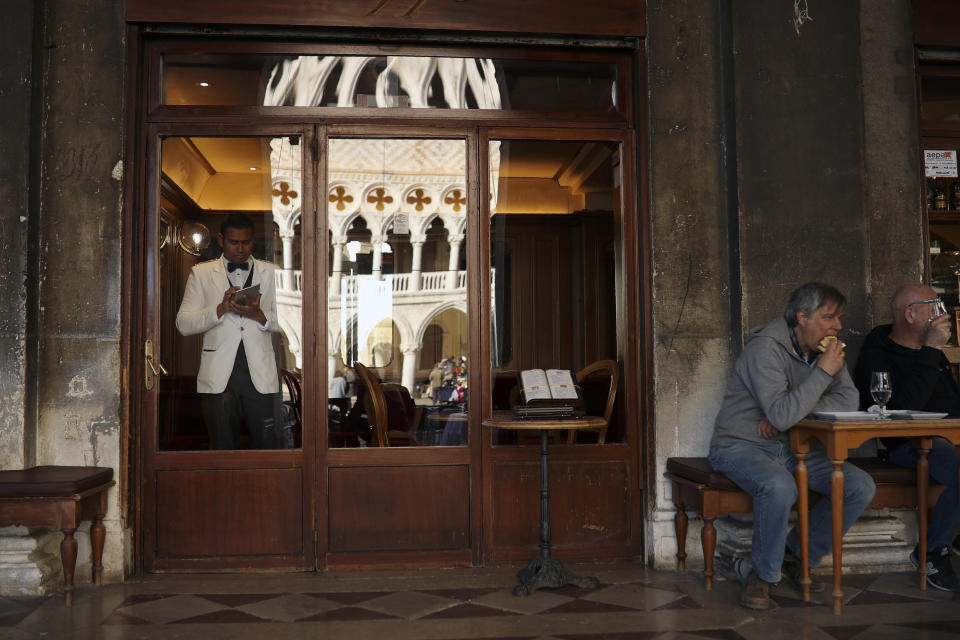 FILE - In this Friday, Feb. 28, 2020 file photo, a waiter waits for customer as locals eat a meal in a restaurant at St. Mark's Square in Venice, Italy. With the coronavirus emergency deepening in Europe, Italy, a focal point in the contagion, risks falling back into recession as foreign tourists are spooked from visiting its cultural treasures and the global market shrinks for prized artisanal products, from fashion to design. (AP Photo/Francisco Seco, File)