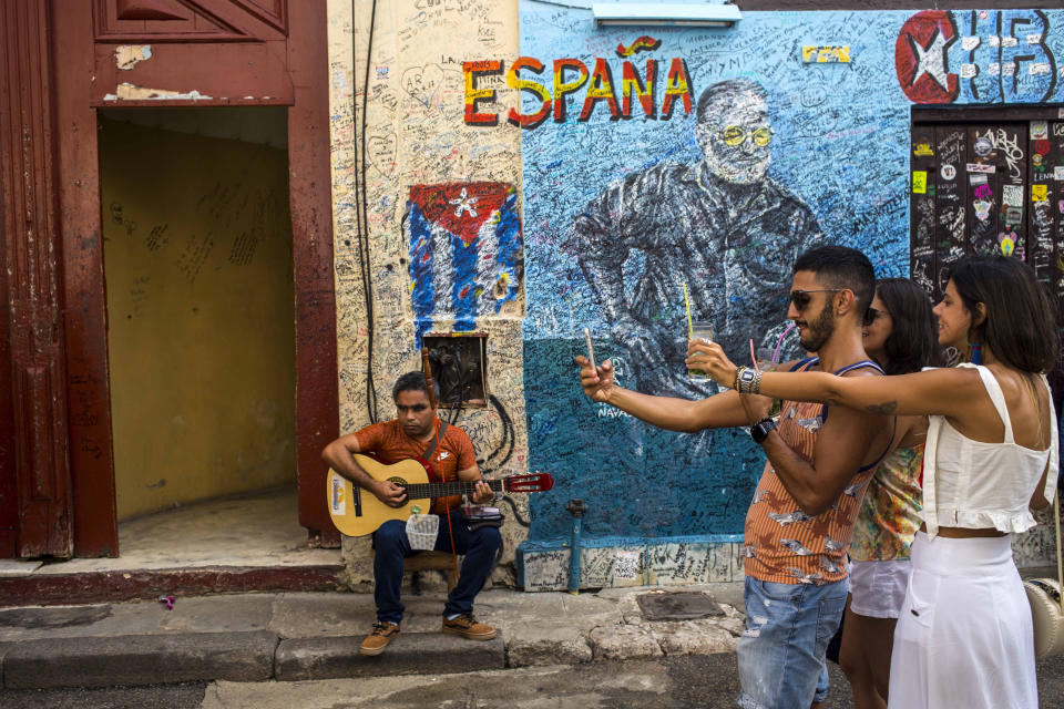 A street musician plays his guitar as tourists take selfies in Havana, Cuba, Wednesday, Dec. 5, 2018. Cuba is softening the impact of a heavily criticized new law that would have given government inspectors power to shut down any exhibition or performance deemed to violate the country's socialist revolutionary values. (AP Photo/Desmond Boylan)