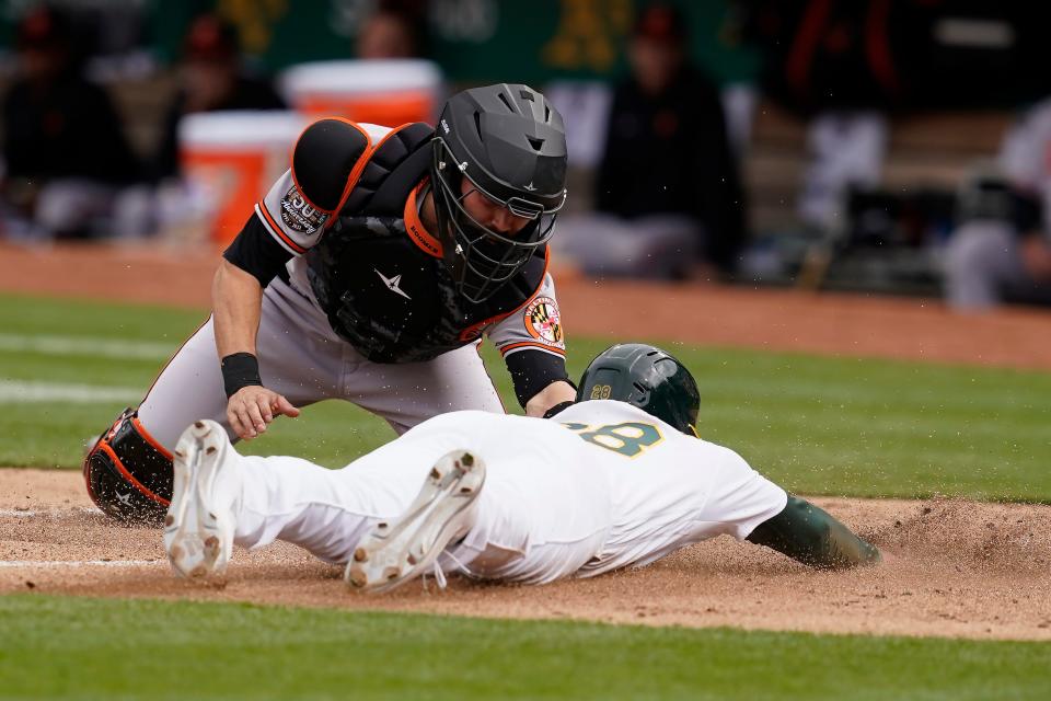 Oakland Athletics' Billy McKinney, bottom, is tagged out at home by Baltimore Orioles catcher Anthony Bemboom during the second inning of a baseball game in Oakland, Calif., Wednesday, April 20, 2022. (AP Photo/Jeff Chiu)