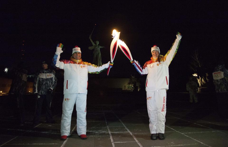 In this photo provided by Olympictorch2014.com, Olympic torch bearers Kamil Larin, left, and Yelena Slesarenko put their torches together during an Olympic torch relay in Volgograd, a city on the Volga River about 800 kilometers (about 500 miles) south of Moscow, Russia, Monday, Jan. 20, 2014 with a monument to Motherland at the background. The 65,000-kilometer (40,389 mile) Sochi torch relay, which started on Oct. 7, is the longest in Olympic history. The torch has traveled to the North Pole on a Russian nuclear-powered icebreaker and has even been flown into space. (AP Photo/Olympictorch2014.com)