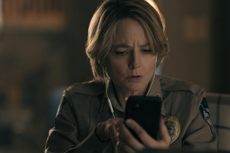 Jodie watching something on a phone with headphones in her ears in a scene from "True Detective"