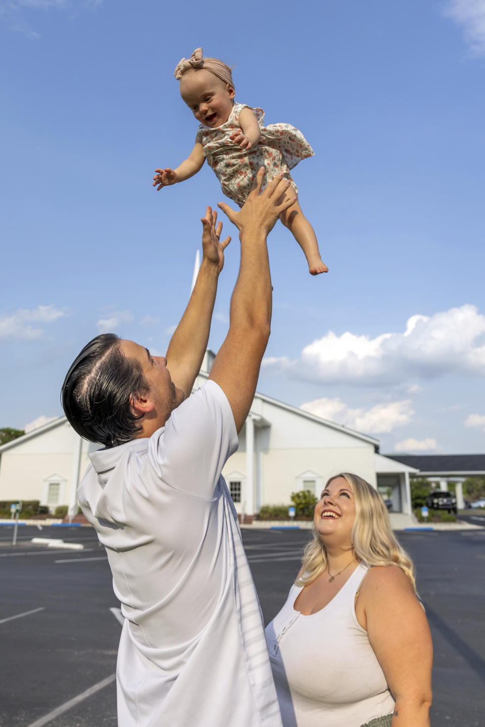 Sam Earle lifts his daughter, Novalie, while his wife, Tori, watches outside the Heritage Baptist Church Tuesday, May 7, 2024, in Lakeland, Fla. Novalie was born through an embryo adoption. (AP Photo/Mike Carlson)