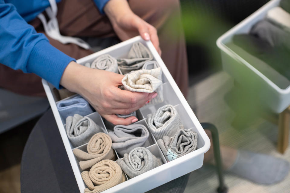 A person is organizing neatly folded socks in a white drawer organizer