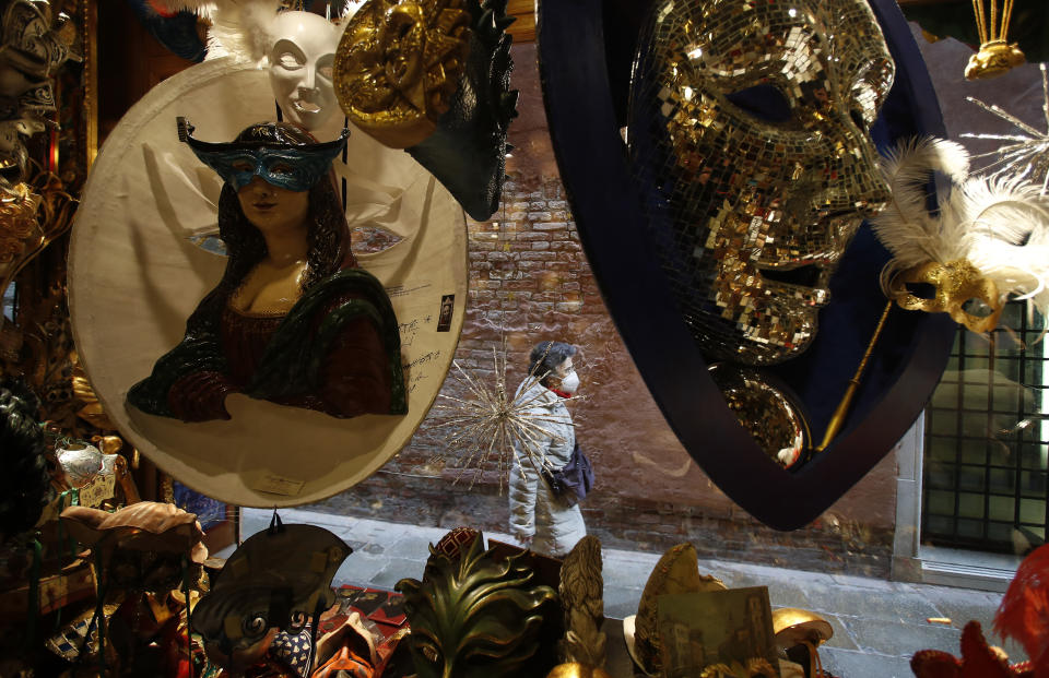 A woman wearing a sanitary mask walks next to a carnival masks shop in Venice, Italy, Saturday, Jan. 30, 2021. Carnival should have begun on Saturday, but the COVID-19 pandemic has made that annual appointment of days of merry-making impossible. (AP Photo/Antonio Calanni)