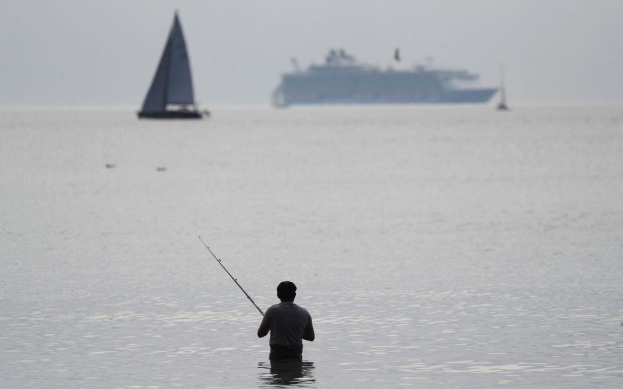 A fisherman fishes in the sea off of Bournemouth beach - Andrew Matthews/PA