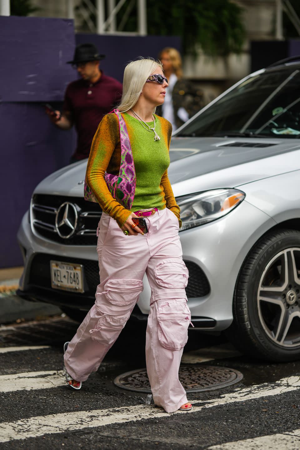 new york, new york september 12 a guest wears black and purple print pattern sunglasses from balenciaga, a green and orange gradient pattern glitter long sleeves t shirt, silver chain pendant necklaces, a pink purple green shiny leather print pattern shoulder bag, a neon pink shiny leather belt, pale pink large cargo pants, silver shiny leather nailed studded sandals from balenciaga, outside carolina herrera, during new york fashion week, on september 12, 2022 in new york city photo by edward berthelotgetty images