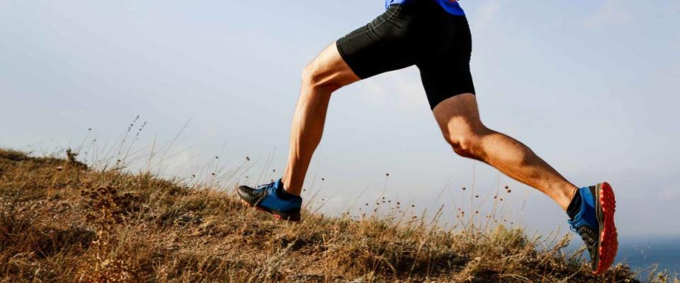 legs male athlete runner running uphill on trail background of sky