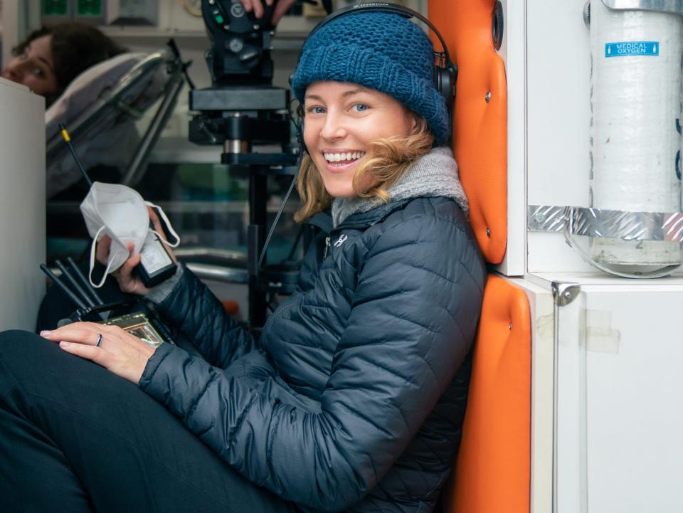 Elizabeth Banks in a coat and cap next to a camera