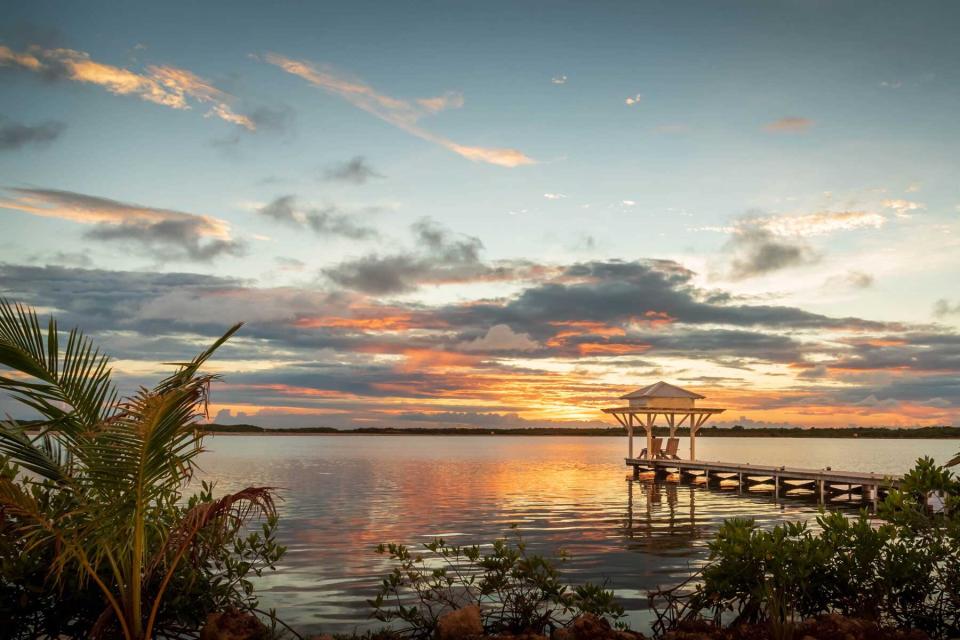 A view of a wooden pier with a bungalow at sunset in the Caribbean.