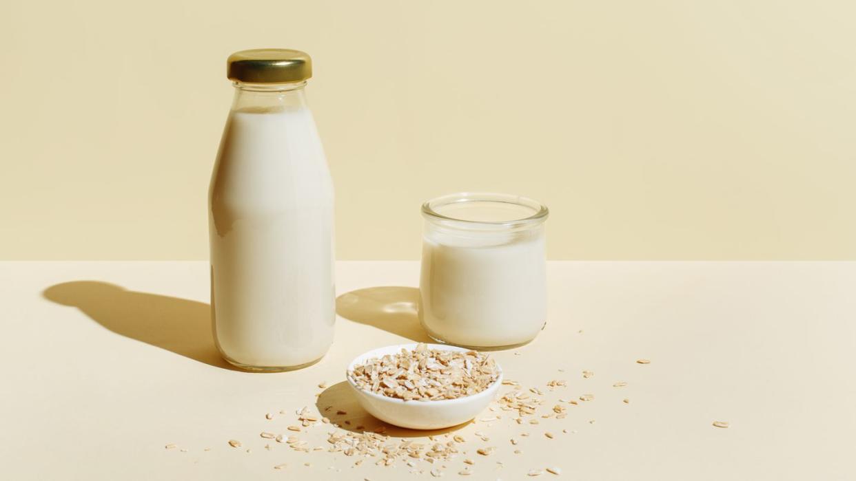 oat milk in glass bottle and glass, oatmeal in a white bowl on beige background healthy vegan non dairy organic drink with flakes lactose free milks in minimal flat lay style top view, copy space
