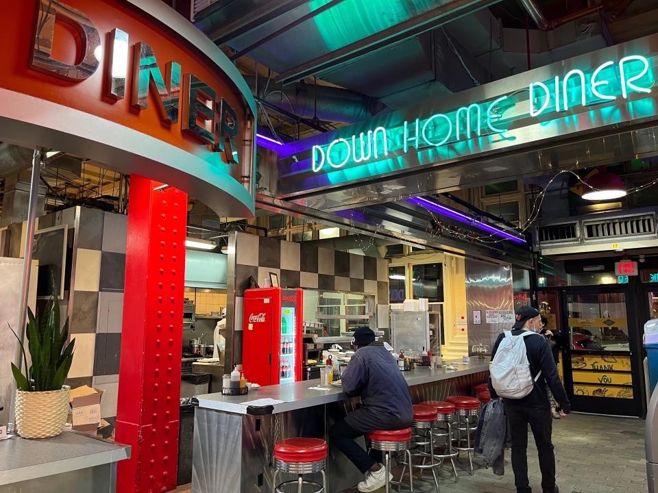 A neon sign that reads "Down Home Diner" above a counter with red stools