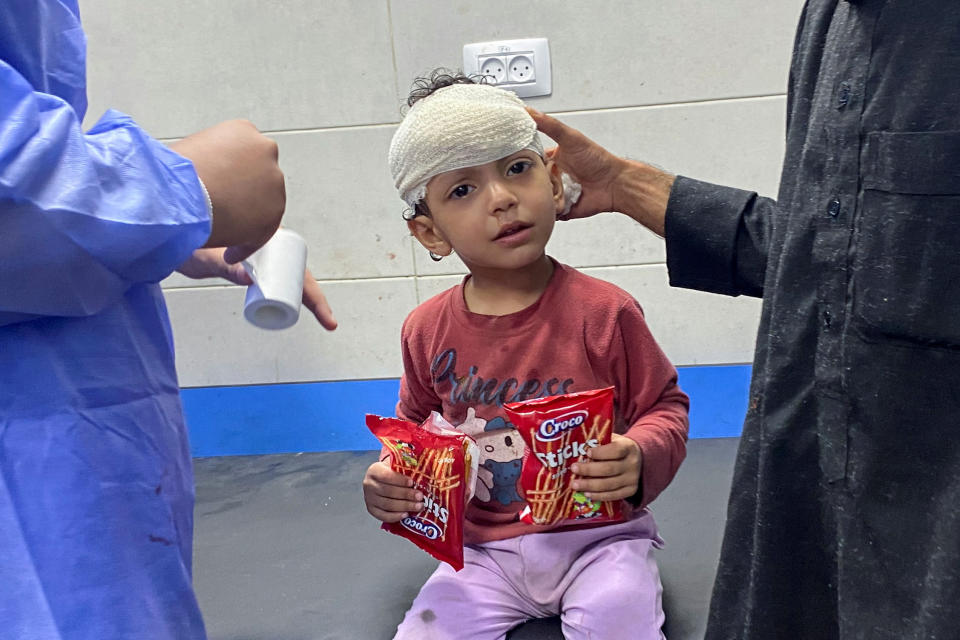 A Palestinian girl who was injured in an Israeli strike is assisted at Shifa Hospital, wearing a head bandage, after having her wounds stitched without anesthesia.