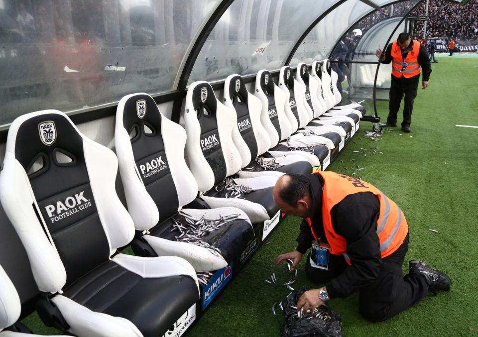 In this photo taken Wednesday, April 16, 2014 an employee of PAOK cleans Olympiakos' bench from fish before a semi-final of the Greek Cup in the northern port city of Thessaloniki. Police in Thessaloniki have arrested a PAOK fan accused of dumping a crate of fish on the visiting Olympiakos bench, in a jibe that delayed a tense Greek cup semi-final for more than an hour. Another six PAOK supporters were arrested during clashes with police before and after Thursday’s match, which PAOK won 1-0 to advance on aggregate. The game was repeatedly halted by on-turf brawls, resulting in three red cards, while PAOK fans in the stands lit thousands of flares, and several were thrown on the pitch. (AP Photo/InTime Sports, Yorgos Matthaios) GREECE OUT