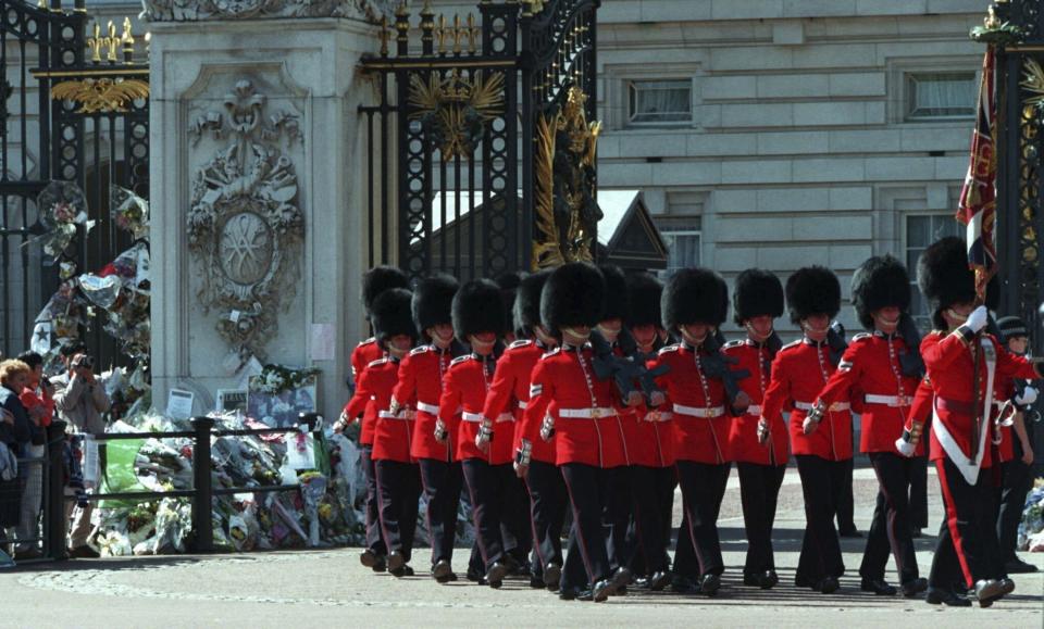 FILE - Tourists watch the changing of the guard outside of Buckingham Palace, Sept. 8, 1997, near floral tributes to the late Princess Diana. When it comes to the United Kingdom's royal family, the Americans can't seem to get enough. Through weddings, divorces, births, deaths, they've been invested in it all. (AP Photo/David Brauchli, File)