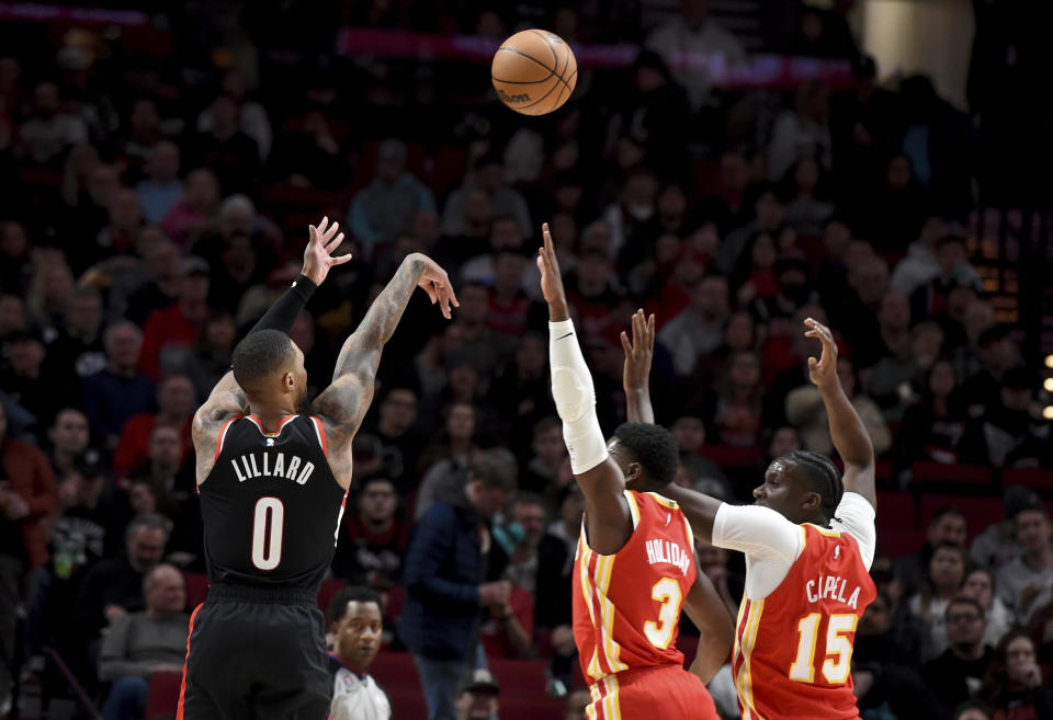 Portland Trail Blazers guard Damian Lillard, left, shoots a basket over Atlanta Hawks guard Aaron Holiday, center, and center Clint Capela, right, during the first half of an NBA basketball game in Portland, Ore., Monday, Jan. 30, 2023. (AP Photo/Steve Dykes)