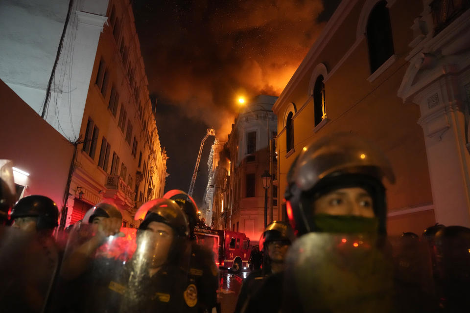 Policías antimotines bloquean una calle mientras un edificio arde a sus espaldas en una jornada de enfrentamientos contra manifestantes opositores en Lima, Perú, el jueves 19 de enero de 2023. (AP Foto/Martín Mejía)