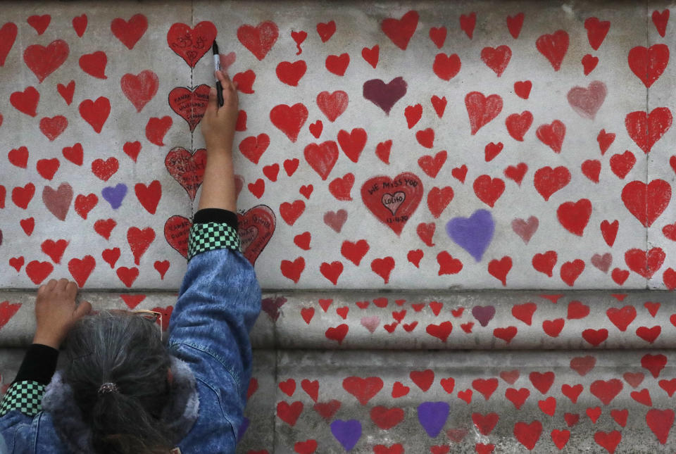 People paint red hearts onto the COVID-19 Memorial Wall mourning those who have died, opposite the Houses of Parliament on the Embankment in London, Monday, April 5, 2021. Hearts are being painted onto the wall in memory of the many thousands of people who have died in the UK from coronavirus. (AP Photo/Frank Augstein)