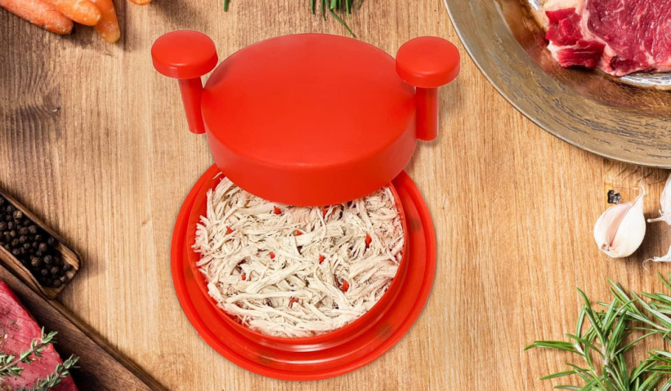 the meat shredder in red surrounded by various cooking ingredients on a wooden table