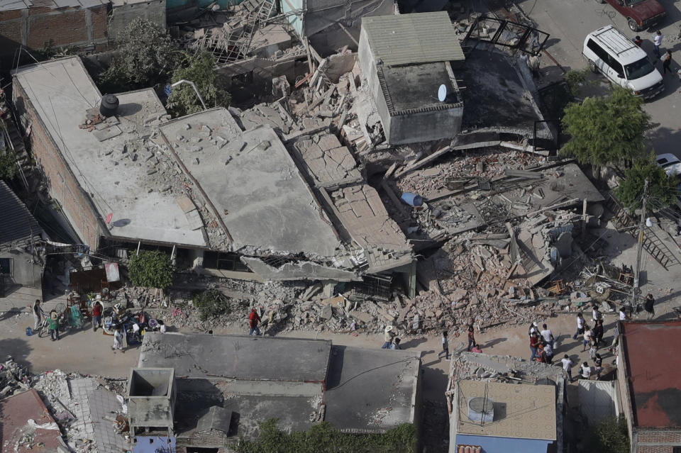 <em>People walk through a neighbourhood where many buildings collapsed in the quake (AP)</em>