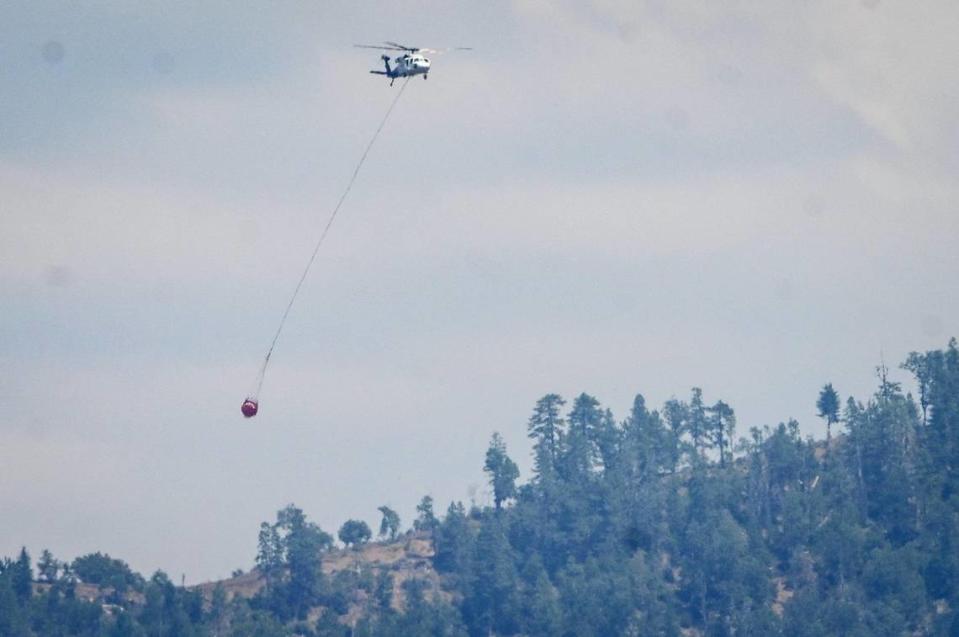 A helicopter flies over a hillside looking to do a water drop on the Oak Fire in Mariposa County on Tuesday, July 25, 2022.
