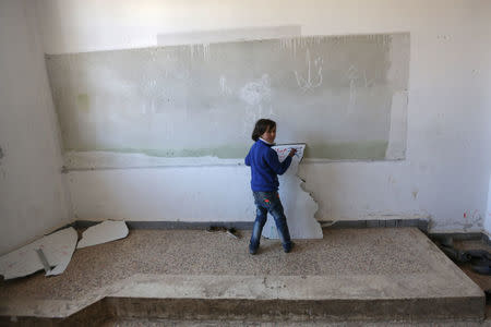 A student writes on a broken whiteboard during a class at the 'Aisha Mother of the BelieversÕ school which was recently reopened after rebels took control of al-Rai town from Islamic State militants, Syria January 16, 2017. Picture taken January 16, 2017. REUTERS/Khalil Ashawi