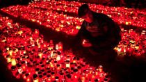 FILE - In this Monday, Nov. 2, 2015 photograph, a riot policeman places a candle, collected from people waiting to pay respects to the victims of a fire, outside the Colectiv nightclub, in Bucharest, Romania. The Oscar-nominated Romanian documentary film “Collective” follows a group of journalists delving into the state of health care in the eastern European country in the wake of a deadly 2015 nightclub fire that left dozens of burned victims in need of complex treatment. What they revealed was decades of deep-rooted corruption, a heavily politicized system scarily lacking in care. (AP Photo/Vadim Ghirda, File)