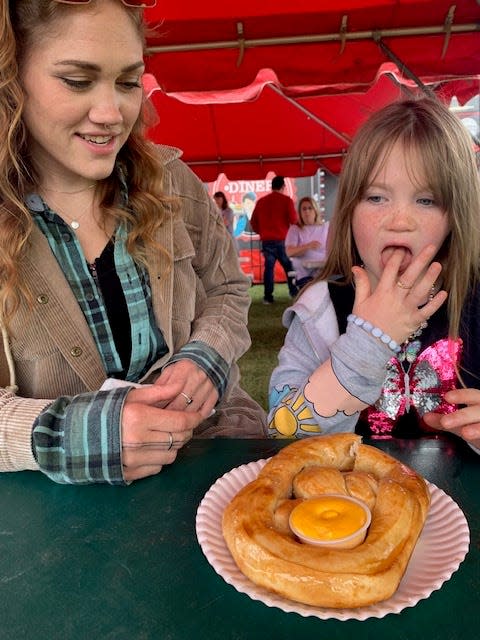 Aurora Trudell, 7, gets ready to dive into a soft pretzel with her mother, Brittany Emmons, during Sunday’s opening day at the 172nd St. Joseph County Grange Fair.