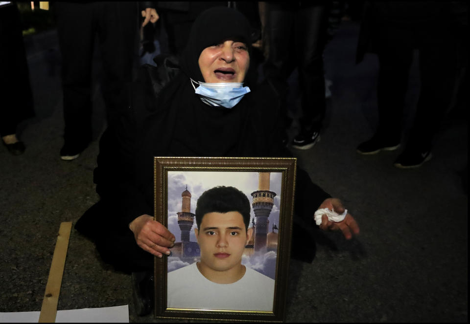 A mother of a victim of the Aug. 4, 2020 Beirut port explosion, sits in the middle of a blocked street as she reacts holding a portrait of her son who killed during the explosion, during a sit-in outside the Justice Palace, in Beirut, Lebanon, Thursday, Feb. 18, 2021. Lebanon's highest court asked the chief prosecutor investigating last year's massive Beirut port explosion to step down, following legal challenges by senior officials he had accused of negligence that led to the blast, a judicial official and the country's official news agency said. (AP Photo/Hussein Malla)