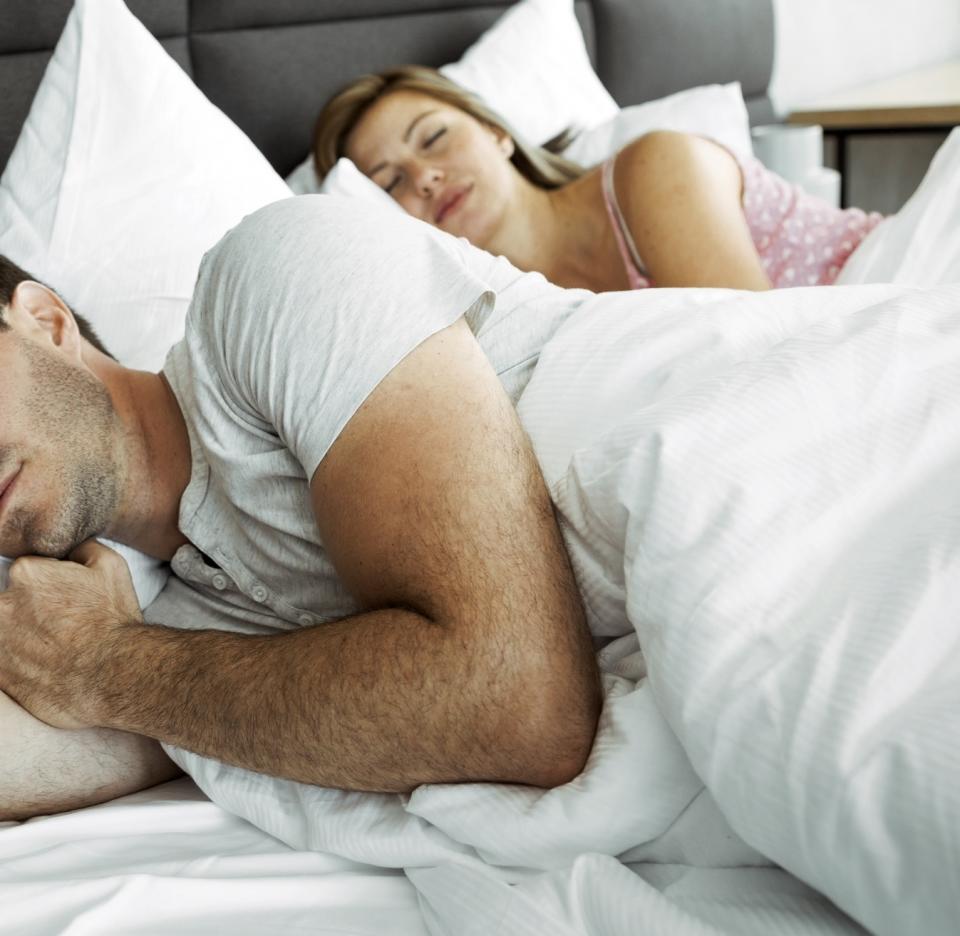 A man and a woman are sleeping side by side in bed. The man is wearing a t-shirt, and the woman is in a pajama top