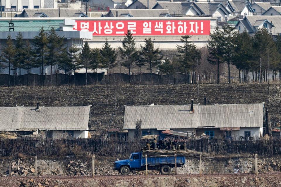 A Korean sign behind some gray buildings, a blue truck, and a group of people.